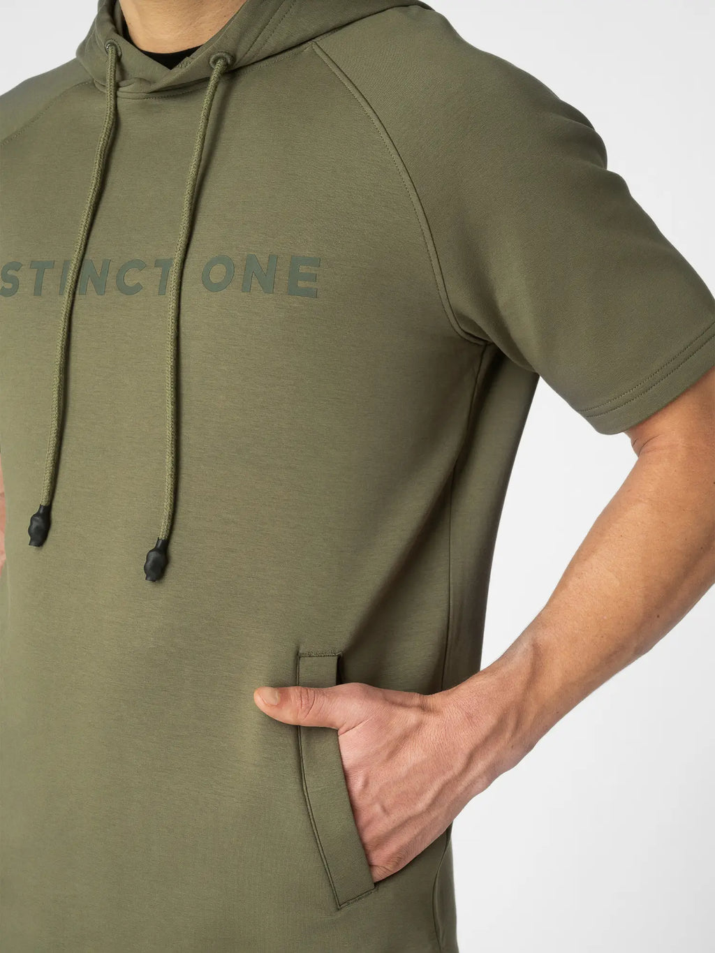 Close-up of a person wearing an olive green short-sleeve hoodie with a tonal 'DISTINCT ONE' logo across the chest and black drawstrings, shown against a light gray background.
