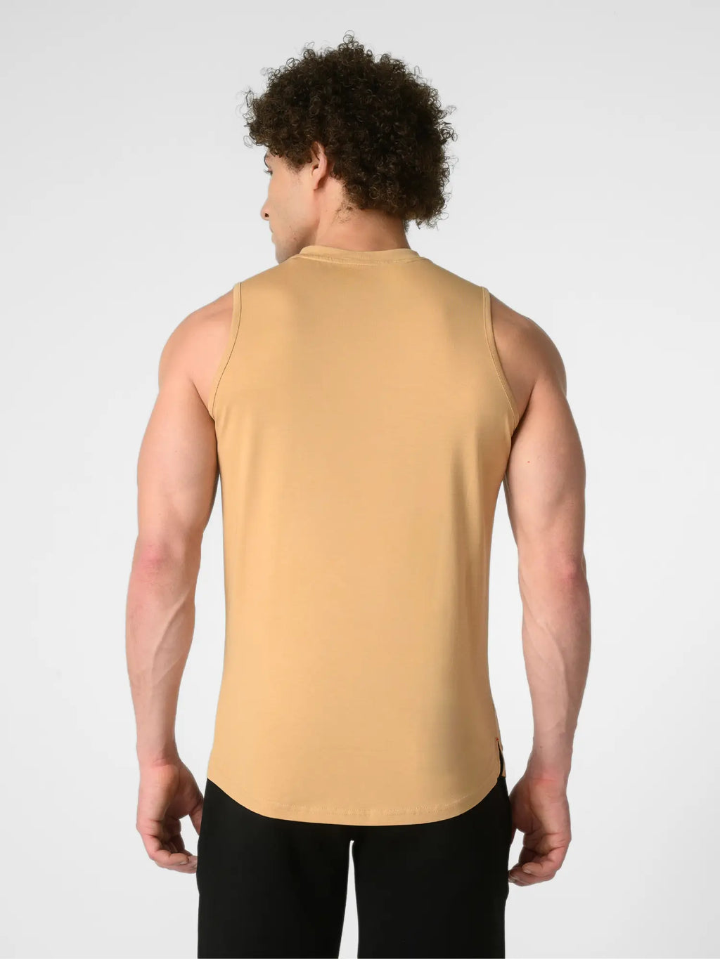 A man viewed from the back wearing a sleeveless, high-neck athletic tank top in a warm camel tan color, paired with black pants, against a light gray studio background.