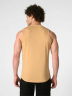A man viewed from the back wearing a sleeveless, high-neck athletic tank top in a warm camel tan color, paired with black pants, against a light gray studio background.