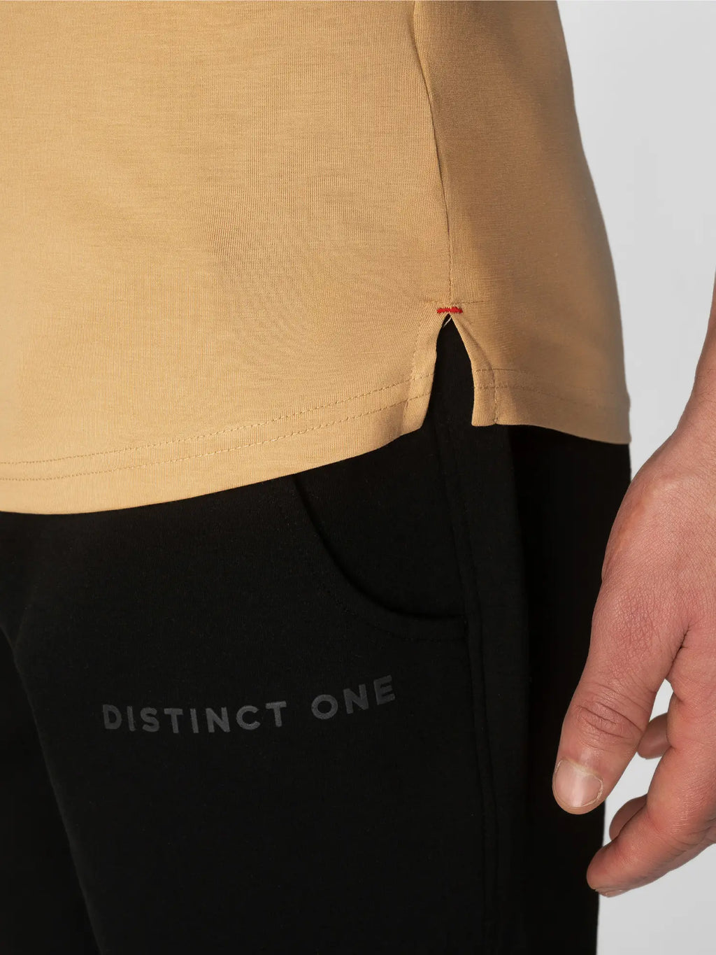 Close-up of a person wearing a tan top and black pants, with the word 'DISTINCT ONE' printed on the thigh and a small red stitch detail at the hem.