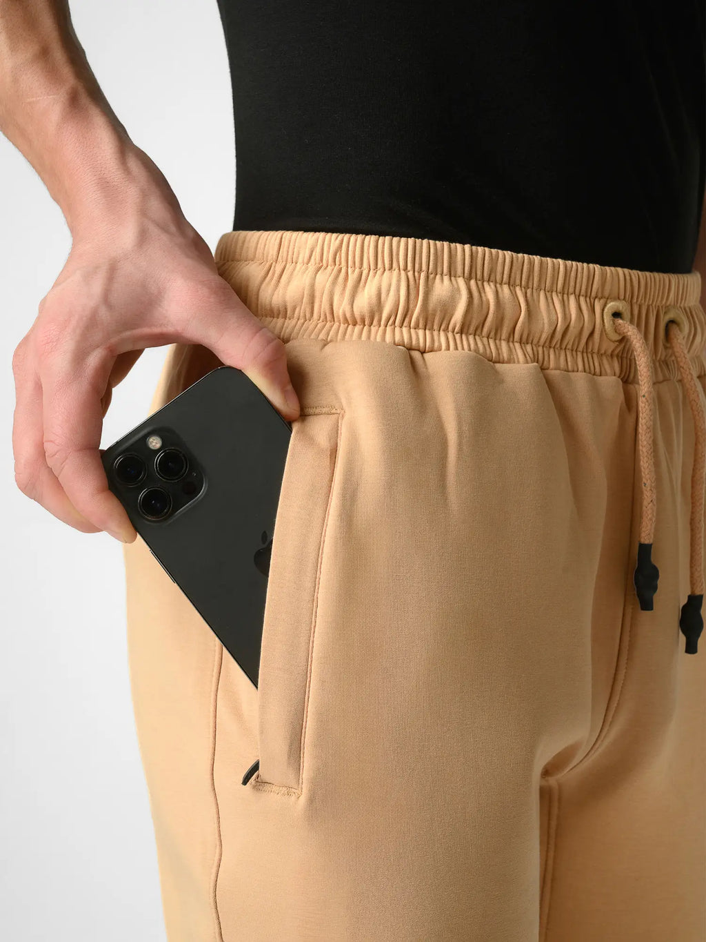 Close-up of a person wearing beige drawstring sweatpants with a black top, showing a hand placing a black smartphone into the side pocket.