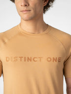 A close-up of a man wearing a tan crewneck athletic t-shirt with the words 'DISTINCT ONE' printed across the chest in a matching tan color.