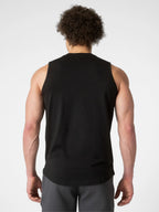 A man viewed from behind wearing a black sleeveless athletic tank top and gray shorts against a light gray studio background.
