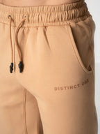 Close-up of beige drawstring sweatpants with a side pocket and the text 'DISTINCT ONE' printed on the thigh.