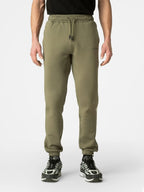 A person wearing olive green jogger sweatpants with a drawstring waist and elastic cuffs, paired with black and white sneakers, shown from the waist down on a light gray studio background.