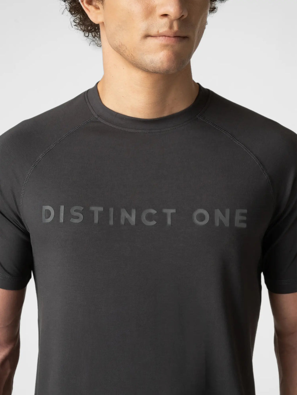A close-up of a man wearing a dark charcoal gray short-sleeve athletic t-shirt with the words 'DISTINCT ONE' printed across the chest in a matching dark gray tone.