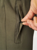 Close-up of a hand opening a zippered pocket on an olive green garment.