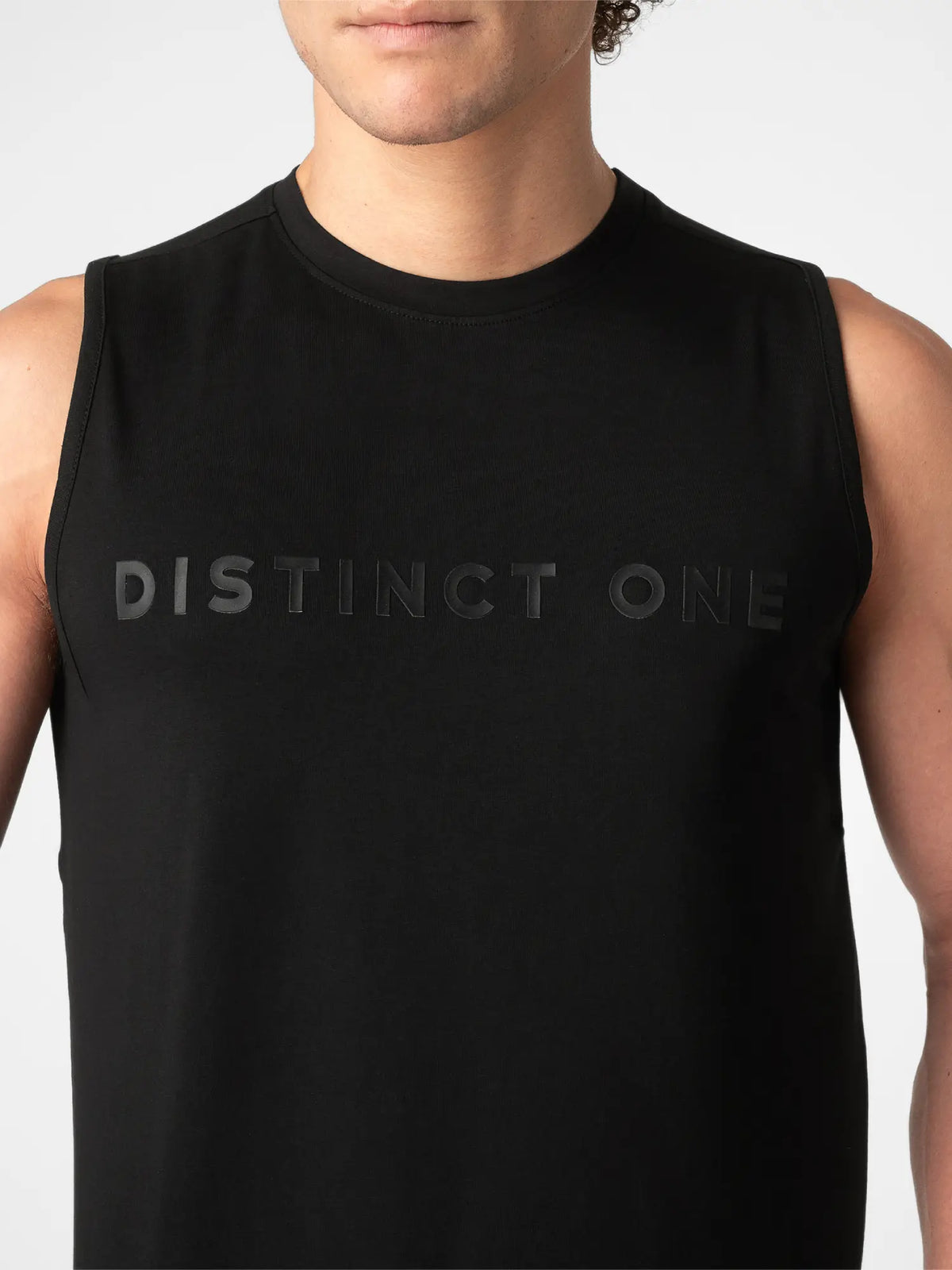 A close-up of a man wearing a black sleeveless muscle tank top with the words 'DISTINCT ONE' printed in a subtle dark gray font across the chest, set against a plain light gray background.