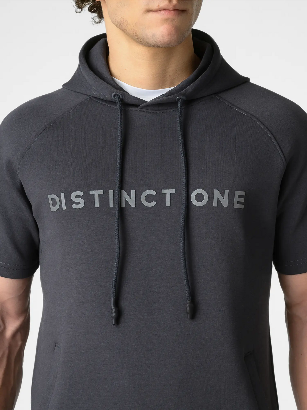 A man wearing a dark gray short-sleeve hoodie with 'DISTINCT ONE' printed across the chest in a matching gray tone, photographed against a light gray studio background.