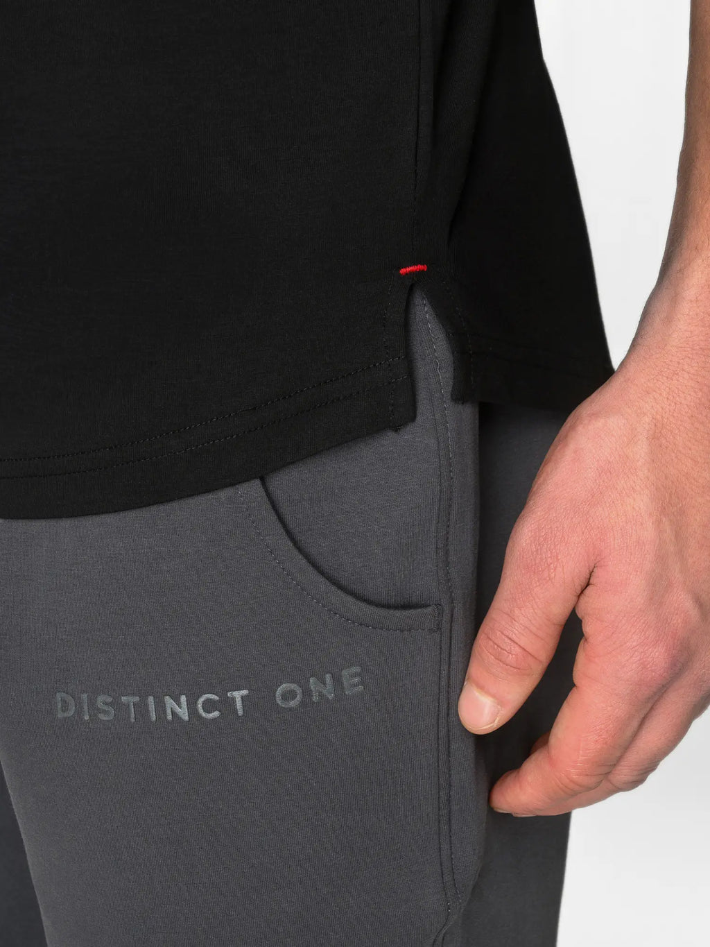 Close-up of a person wearing dark gray Distinct One athletic pants with a side pocket and a black top, showing the brand name on the thigh.