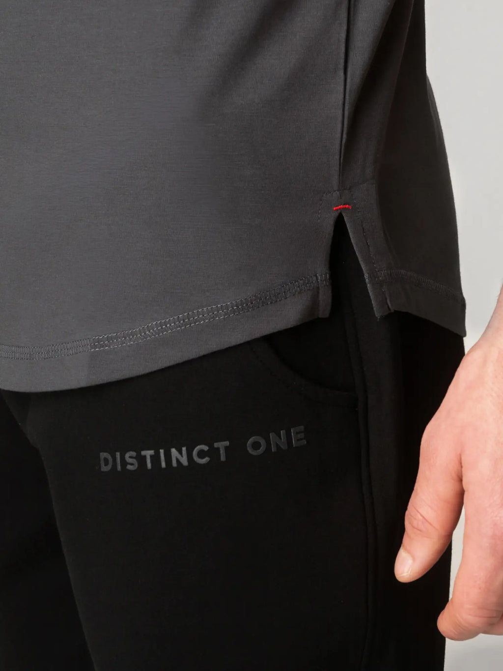 Close-up of a person wearing a dark gray top and black pants with 'DISTINCT ONE' printed on the thigh, against a light gray background.