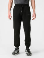 A person wearing black jogger sweatpants with a drawstring waist and elastic cuffs, paired with black and white sneakers, shown against a light gray studio background.