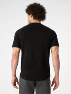 A man viewed from behind wearing a black short-sleeve athletic t-shirt and gray athletic pants against a light gray studio background.
