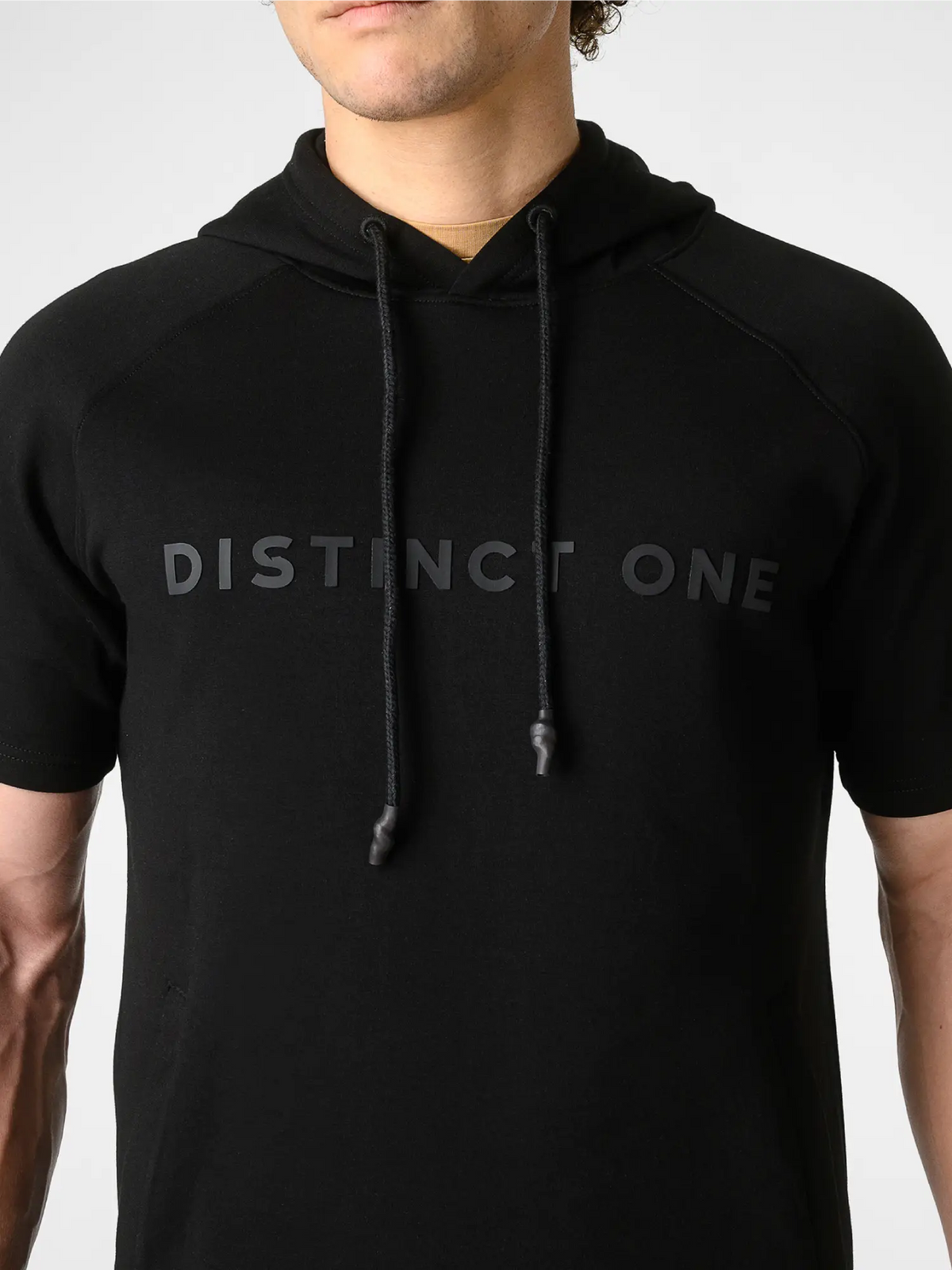 A man wearing a black short-sleeve hoodie with 'DISTINCT ONE' printed in tonal black lettering across the chest, shown against a light gray background.
