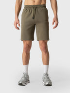 A model from the waist down wearing olive green athletic shorts, white crew socks, and silver sneakers against a light gray studio background.