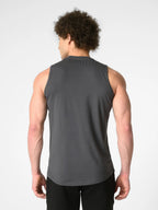 A man viewed from behind wearing a dark gray sleeveless athletic tank top and black pants, standing against a light gray studio background.