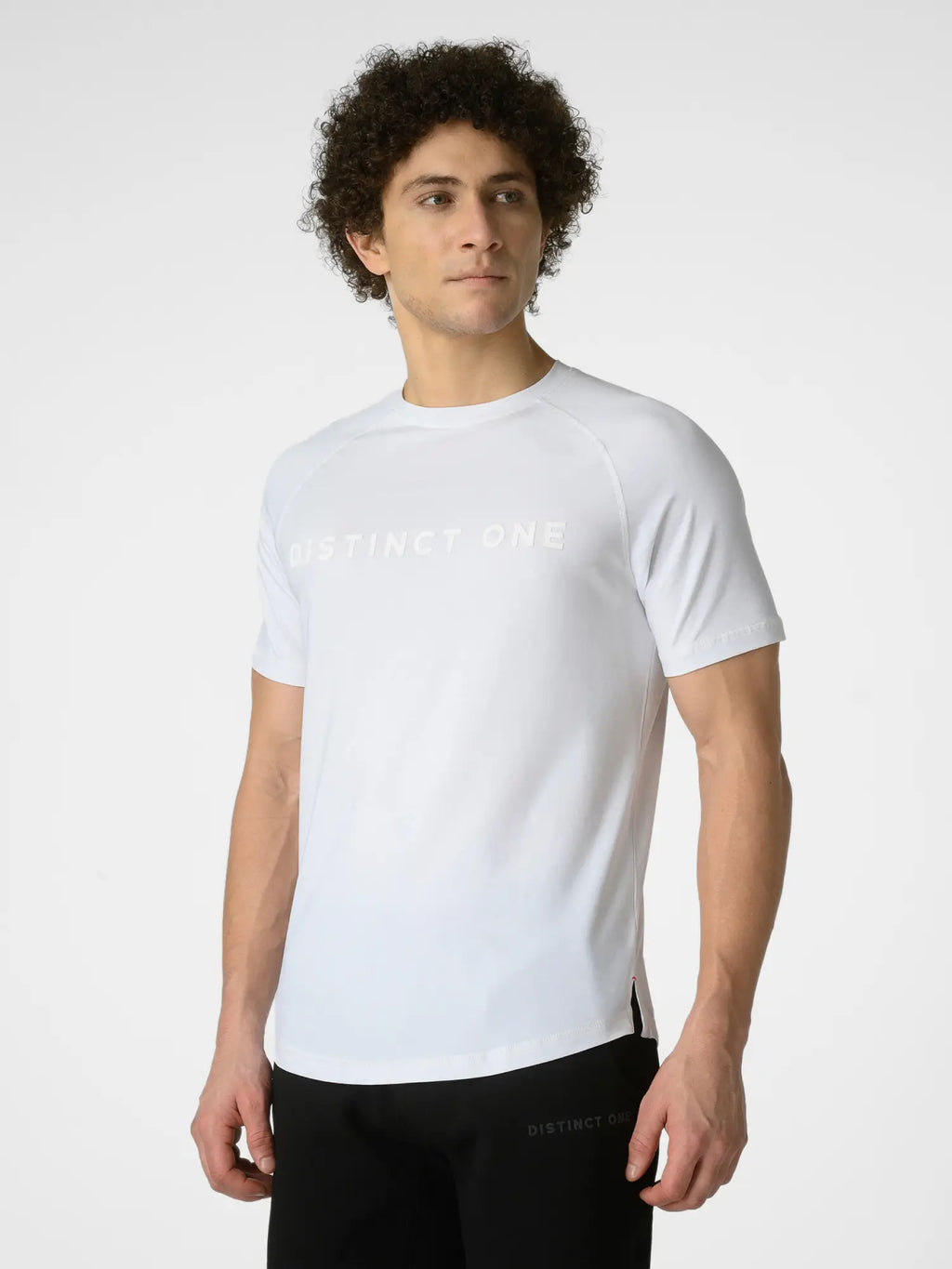 A man wearing a white short-sleeve athletic t-shirt with 'DISTINCT ONE' printed in tonal lettering across the chest, paired with black athletic pants, against a light gray studio background.