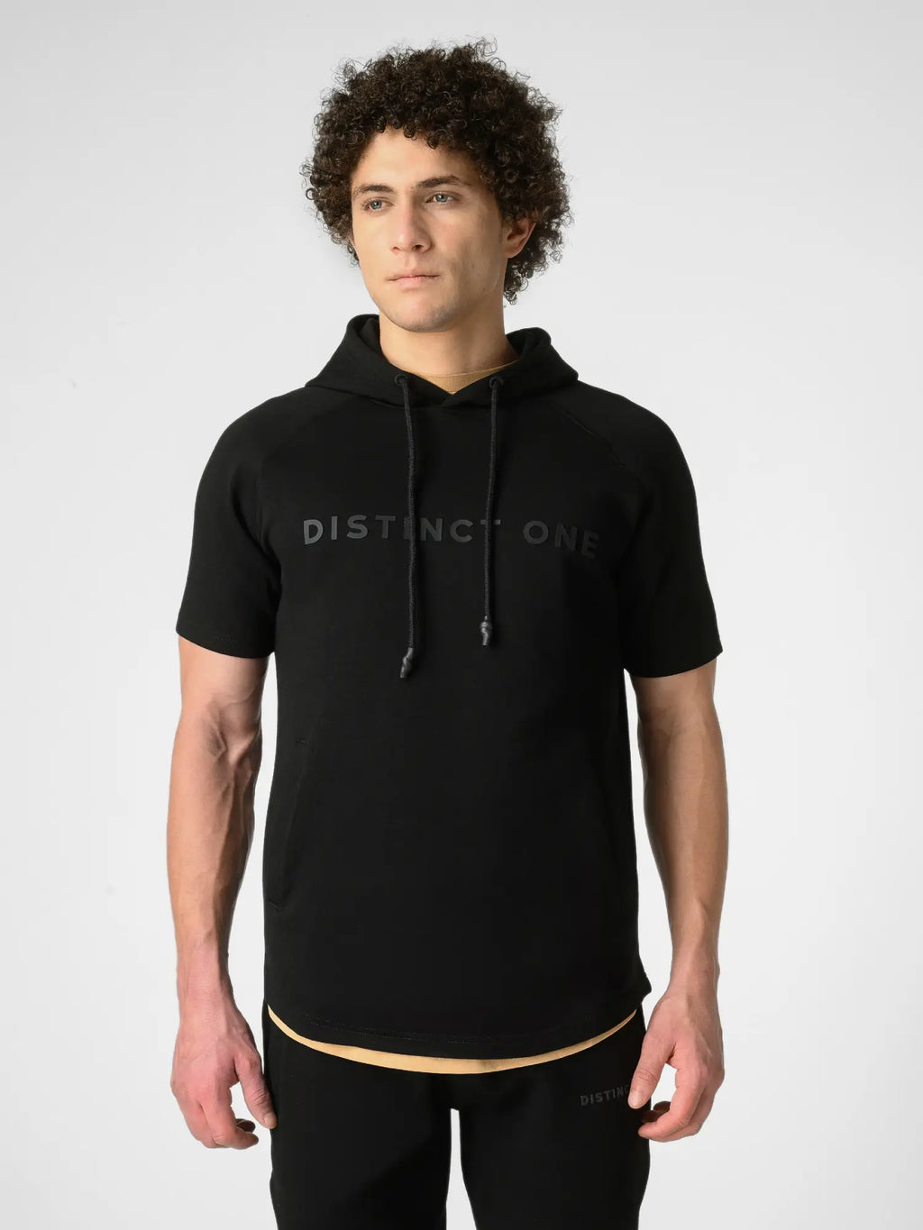A man wearing a black short-sleeve hoodie with 'DISTINCT ONE' printed in gray across the chest, paired with black athletic pants, against a light gray studio background.