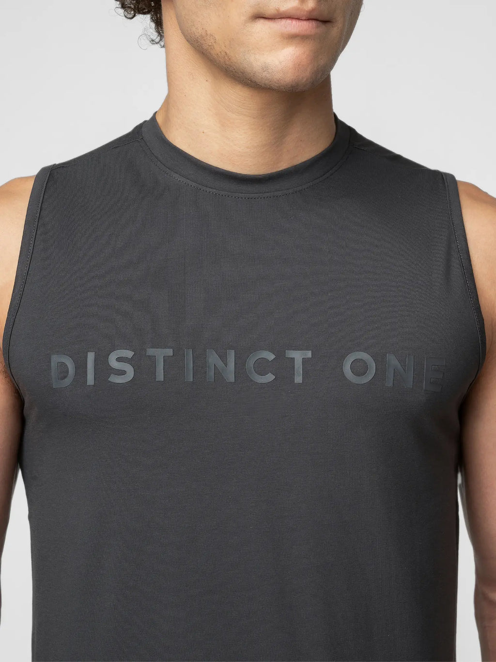A close-up of a man wearing a dark gray sleeveless athletic tank top with the words 'DISTINCT ONE' printed across the chest in a matching dark gray tone.