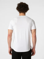 A man viewed from behind wearing a white short-sleeve athletic t-shirt and black pants, set against a plain light gray studio background.