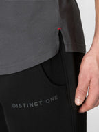 Close-up of a person wearing a dark gray short-sleeve top and black pants with 'DISTINCT ONE' printed on the thigh, showing a hand and part of the torso against a light gray background.