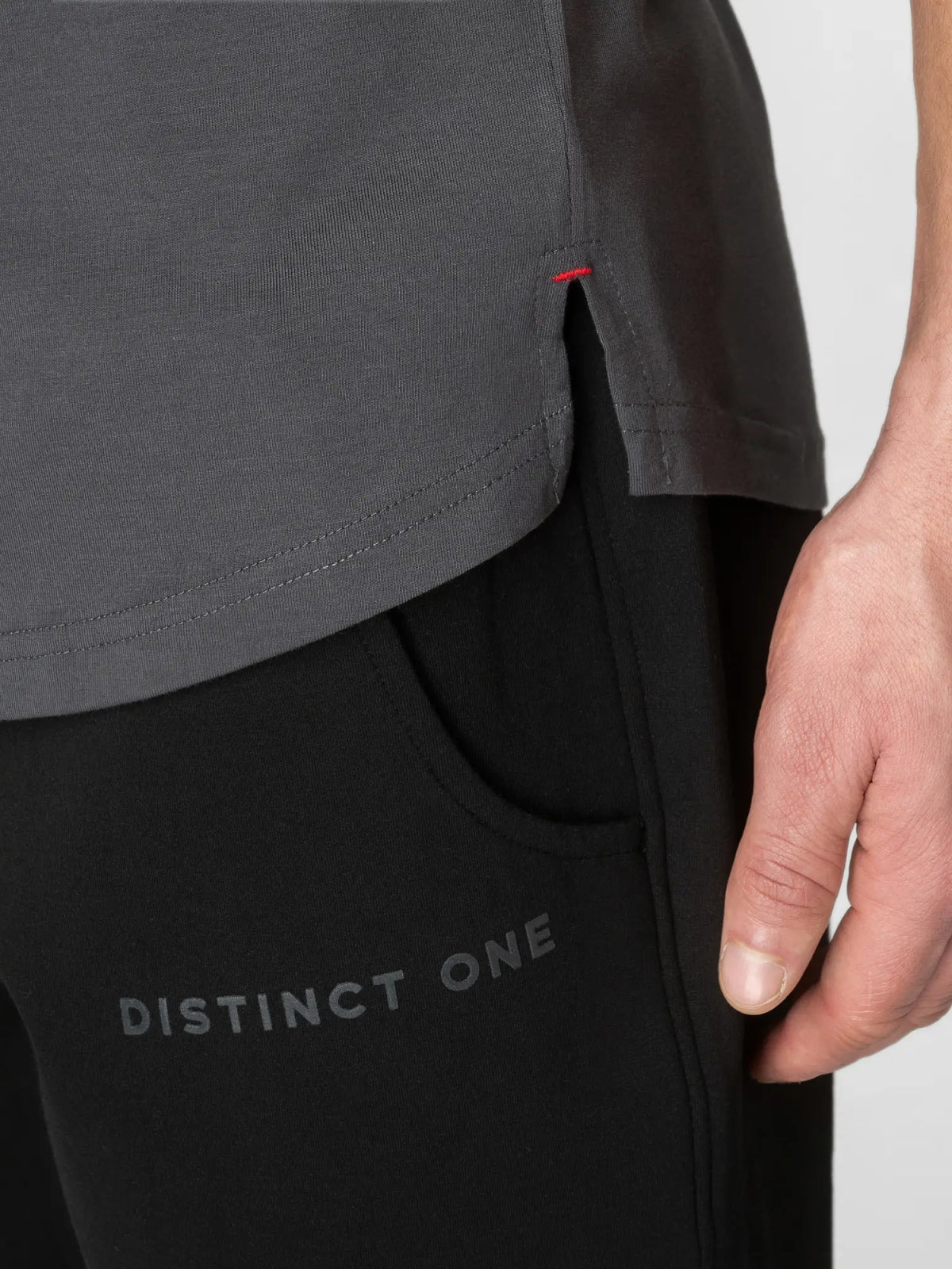 Close-up of a person wearing a dark gray short-sleeve top and black pants with 'DISTINCT ONE' printed on the thigh, showing a hand and part of the torso against a light gray background.