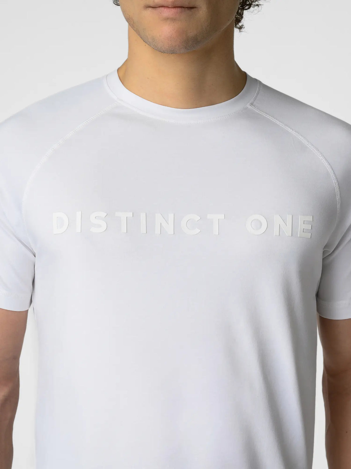 A close-up of a man wearing a white short-sleeve athletic t-shirt with 'DISTINCT ONE' printed across the chest in a matching white tone.