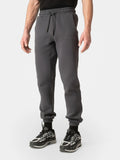 A person wearing dark gray jogger sweatpants with an elastic waistband and drawstring, paired with black and gray sneakers, shown from the waist down on a light gray studio background.