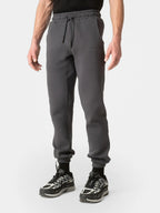 A person wearing dark gray jogger sweatpants with an elastic waistband and drawstring, paired with black and gray sneakers, shown from the waist down on a light gray studio background.