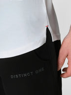 Close-up of a person wearing black athletic pants with 'DISTINCT ONE' printed on the thigh, paired with a white top. A hand is visible pulling the side hem of the shirt.