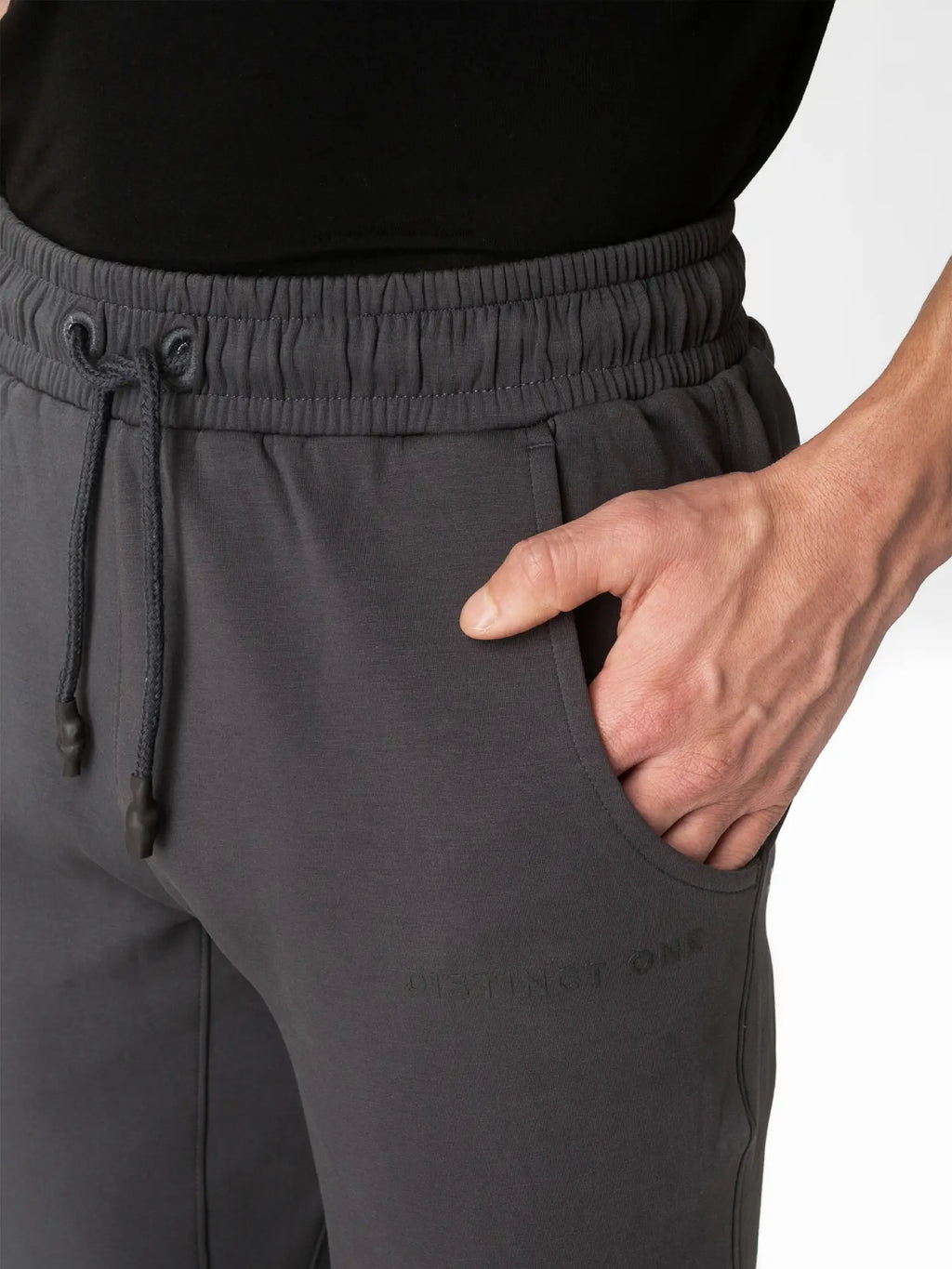 Close-up of a person wearing dark gray drawstring sweatpants with a side pocket, hand in pocket, against a white background.