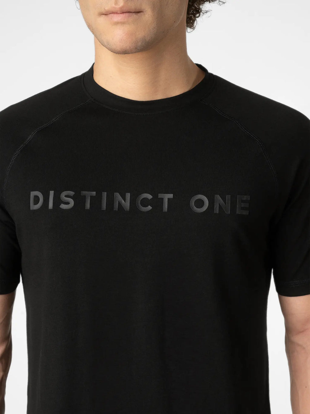 A close-up of a man wearing a black short-sleeve athletic t-shirt with the words 'DISTINCT ONE' printed across the chest in a subtle dark gray tone.