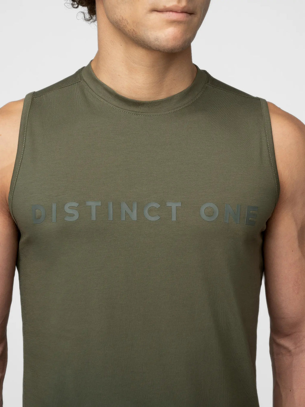 A close-up of a man wearing an olive green sleeveless muscle tank top with the words 'DISTINCT ONE' printed across the chest in a matching dark gray tone.