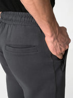 Close-up of a person wearing dark charcoal gray jogger pants, showing the side pocket, elastic waistband, and hand in the pocket.