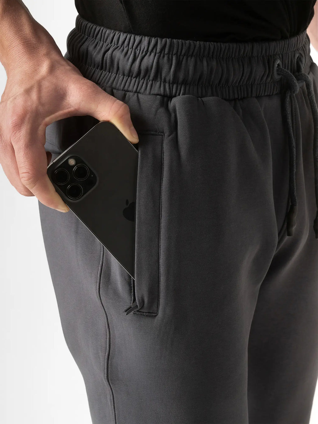 Close-up of a person wearing dark gray drawstring sweatpants, holding a black smartphone in the side pocket.