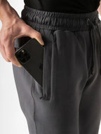 Close-up of a person wearing dark gray drawstring sweatpants, holding a black smartphone in the side pocket.
