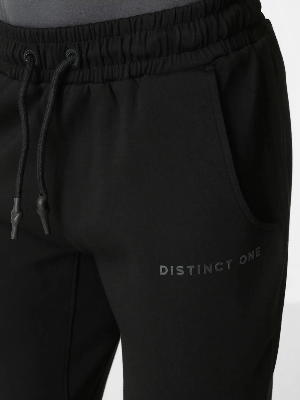 Close-up of black sweatpants with an elastic drawstring waistband, side pocket, and subtle 'DISTINCT ONE' text logo on the lower left leg.