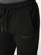 Close-up of black sweatpants with an elastic drawstring waistband, side pocket, and subtle 'DISTINCT ONE' text logo on the lower left leg.