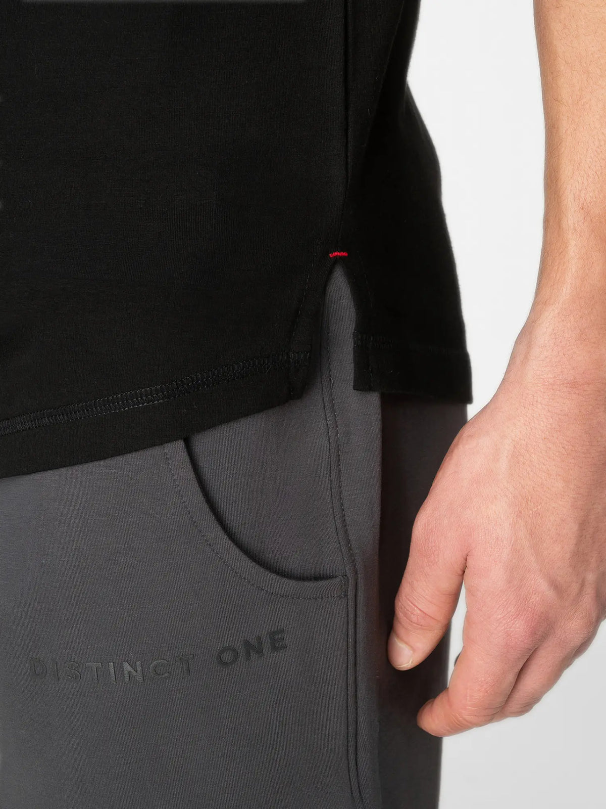 Close-up of a person wearing a black top and dark gray athletic pants with a side pocket and the text 'DISTINGUISH ONE' on the leg.