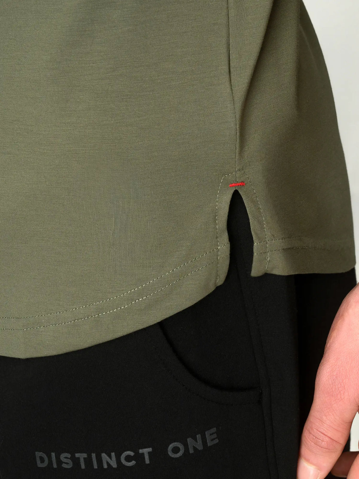 Close-up of a person wearing an olive green short-sleeve top with a side slit, paired with black pants featuring the text 'DISTINCT ONE'.