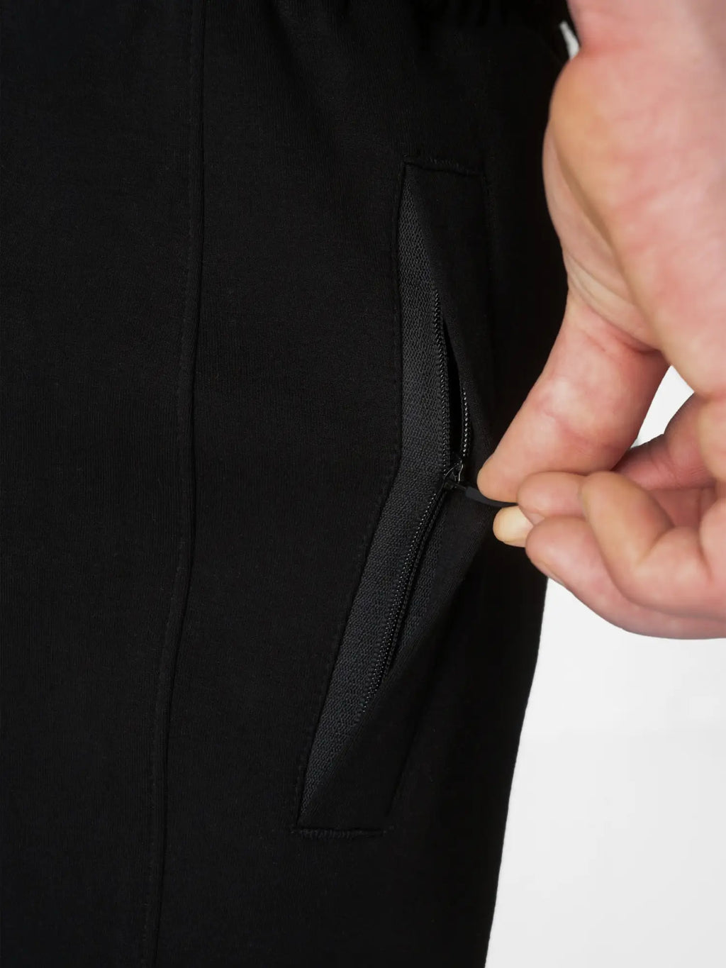 Close-up of a person's hand unzipping a black side pocket on a black garment, with a plain white background visible at the right edge.