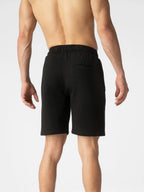 Rear view of a man wearing black athletic shorts against a light gray studio background.