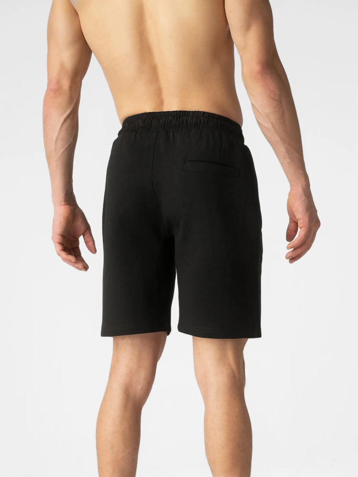 Rear view of a man wearing black athletic shorts against a light gray studio background.