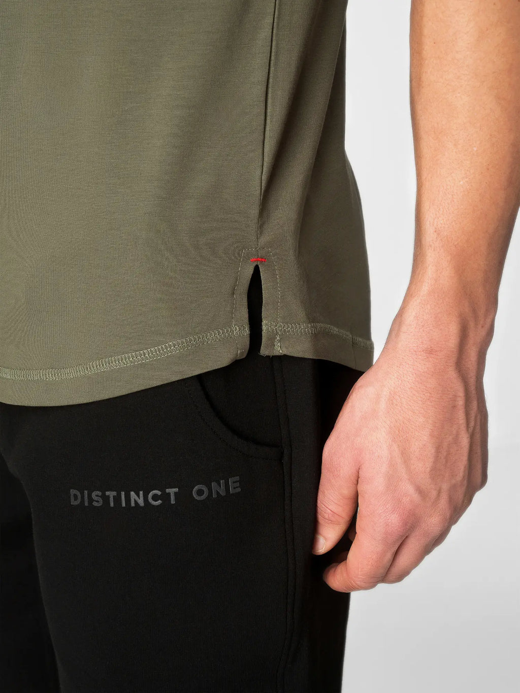 Close-up of a person wearing an olive green athletic top and black pants with 'DISTINCT ONE' printed on the thigh, against a light gray background.