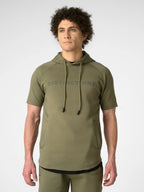 A man wearing an olive green short-sleeve hoodie with 'DISTINCTONE' printed across the chest, paired with matching olive green pants, photographed against a light gray studio background.
