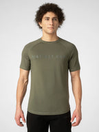 A man wearing an olive green short-sleeve athletic t-shirt with 'DISTINCT ONE' printed across the chest in a subtle, tonal font, paired with black athletic pants, against a light gray studio background.