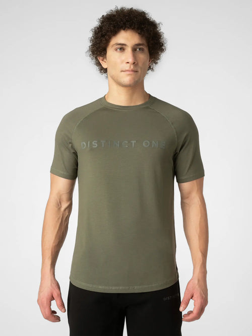 A man wearing an olive green short-sleeve athletic t-shirt with 'DISTINCT ONE' printed across the chest in a subtle, tonal font, paired with black athletic pants, against a light gray studio background.
