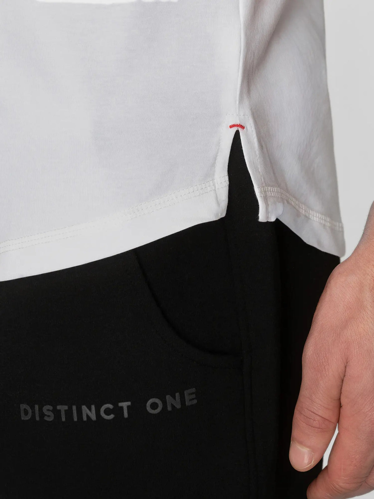 Close-up of a person wearing a white top and black pants with 'DISTINCT ONE' printed on the leg, showing a hand and part of the body.