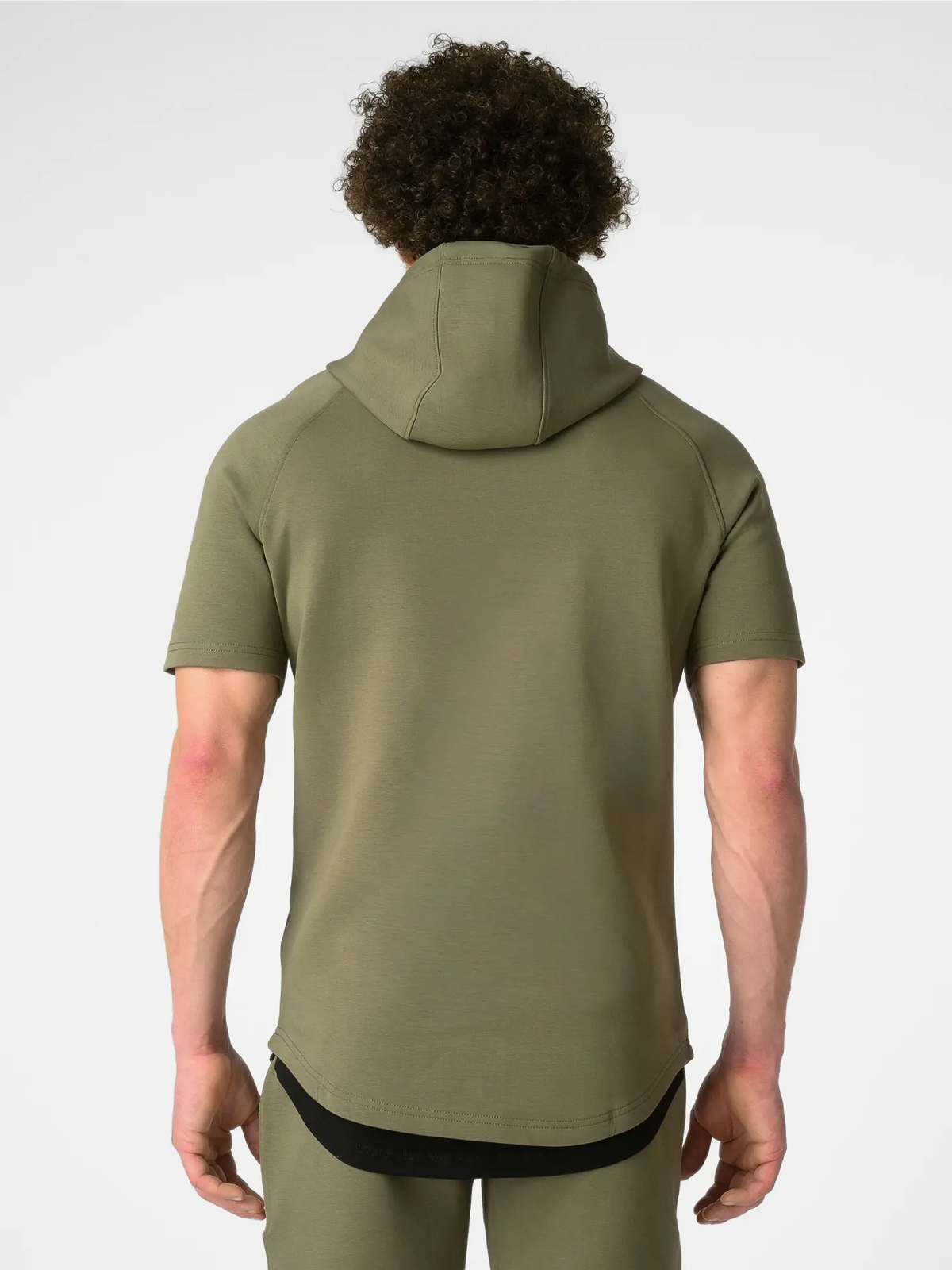 A man viewed from behind wearing a short-sleeve olive green hooded athletic shirt and matching green pants against a light gray studio background.