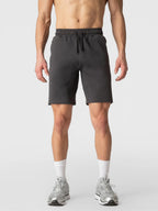 A man wearing dark gray athletic shorts, white socks, and gray sneakers, shown from the waist down against a light gray studio background.